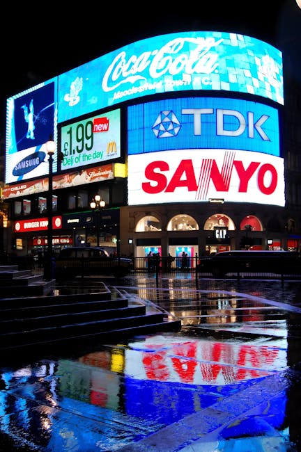 A bright red double-decker bus, marked with the number 38, is positioned on a busy street near Piccadilly Circus at night, with illuminated digital billboards displaying advertisements and video conte